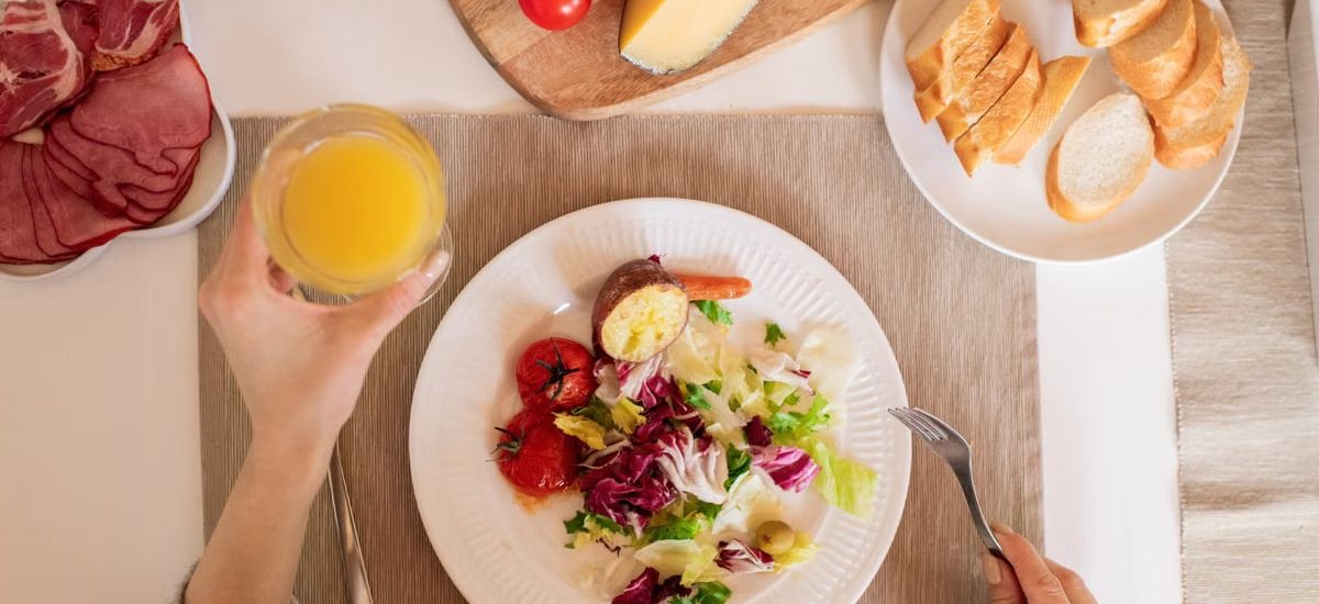 A top-view of a delicious breakfast setting featuring a salad, bread, cheese, tomatoes, and orange juice.