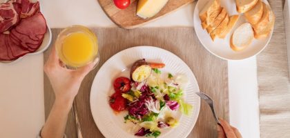 A top-view of a delicious breakfast setting featuring a salad, bread, cheese, tomatoes, and orange juice.