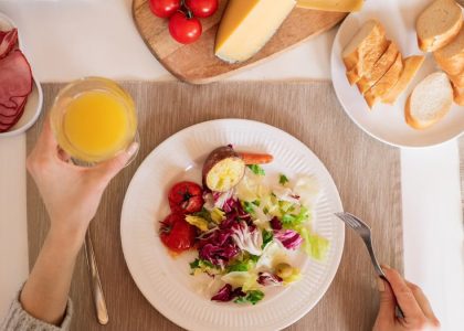 A top-view of a delicious breakfast setting featuring a salad, bread, cheese, tomatoes, and orange juice.